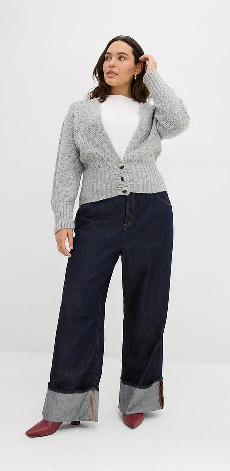 Grå stickad cardigan över vit topp, mörka jeans med uppvik och röda skor.

