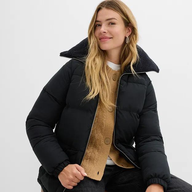 Svart vinterjacka med h&ouml;g krage &ouml;ver en beige stickad tr&ouml;ja och vit t-shirt.

