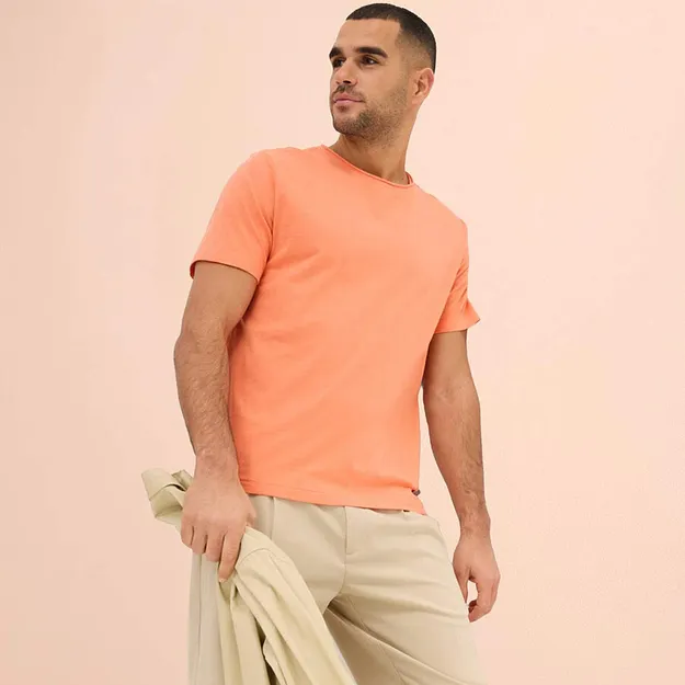 Persikof&auml;rgad T-shirt kombinerad med ljusa byxor och matchande tr&ouml;ja som accessoar.

