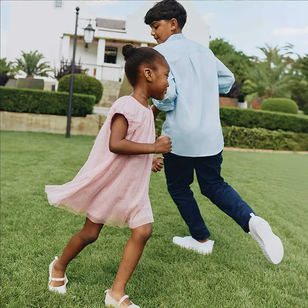 Ett barn i en rosa kl&auml;nning dansar glatt i tr&auml;dg&aring;rden.

