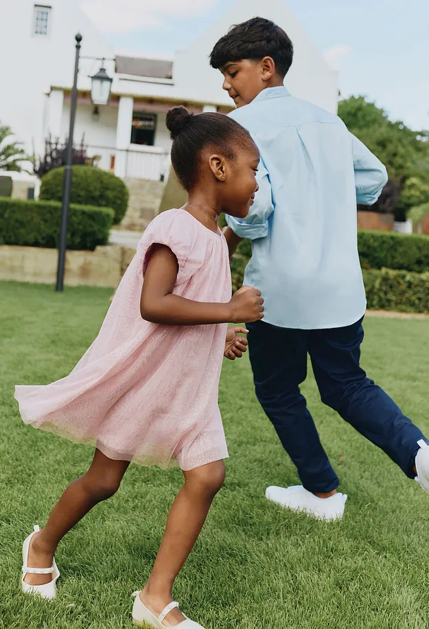 Ett barn i en rosa kl&auml;nning dansar glatt i tr&auml;dg&aring;rden.

