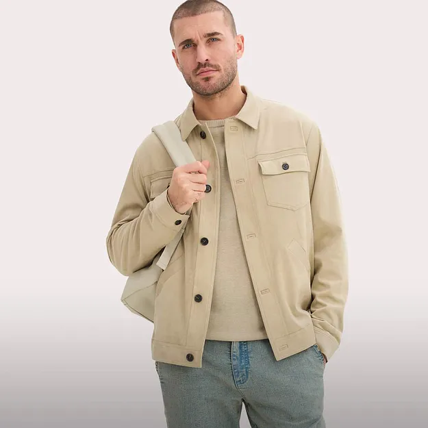 Beige jacka med knappar och br&ouml;stficka &ouml;ver ljus tr&ouml;ja. Till det bl&aring; jeans.

