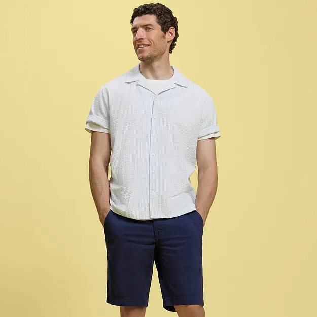En man har p&aring; sig en vit kort&auml;rmad skjorta och m&ouml;rkbl&aring; shorts.

