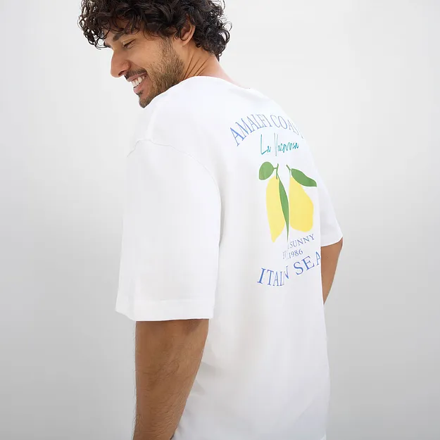 Vit T-shirt med citronmotiv och text p&aring; ryggen.

