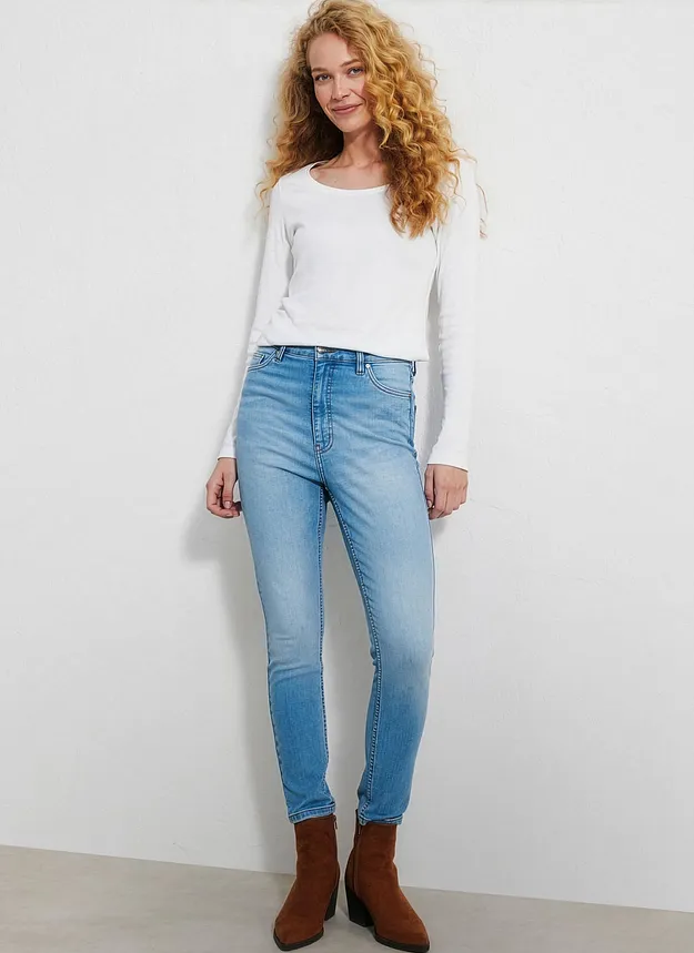 Hon har p&aring; sig en enkel, vit &ouml;verdel, ljusa jeans och bruna st&ouml;vletter.
