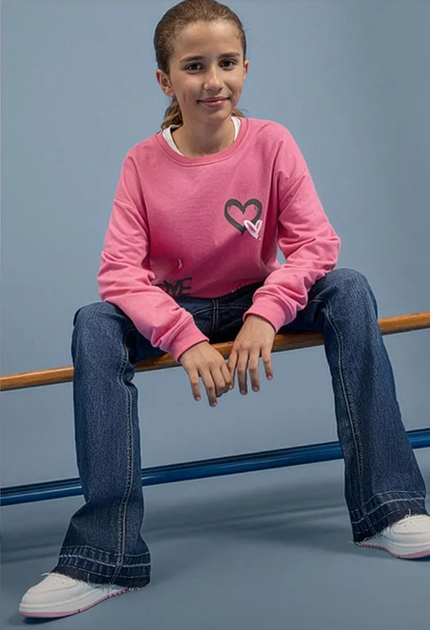 Moderiktig outfit: rosa, l&aring;ng&auml;rmad topp med hj&auml;rtan, vida jeans och bekv&auml;ma vita sneakers.