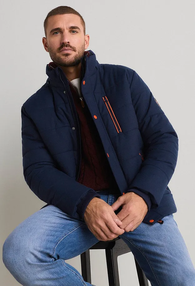 M&ouml;rkbl&aring; t&auml;ckjacka med orangea detaljer, r&ouml;d, stickad tr&ouml;ja och ljusa jeans.