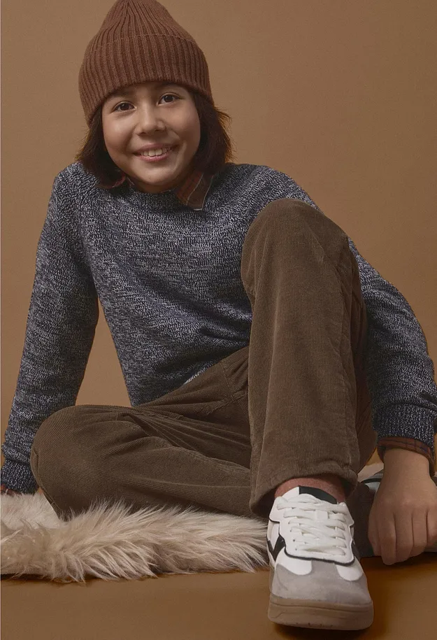 En flicka har p&aring; sig en brun m&ouml;ssa, en rosa tr&ouml;ja, bl&aring;a jeans och vita sneakers.