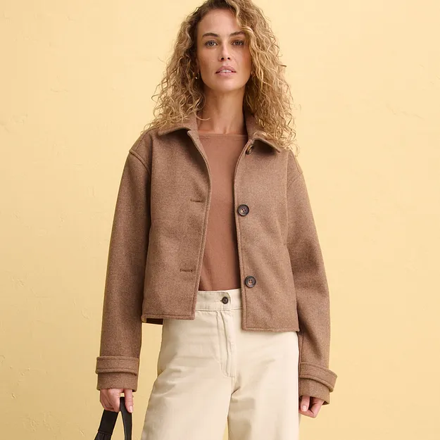 Elegant brun kort jacka &ouml;ver en skir topp, kombinerat med ljusa byxor.

