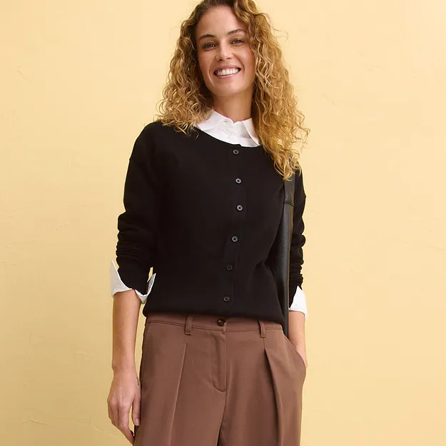 Svart cardigan med kn&auml;ppning &ouml;ver vit blus, tillsammans med bruna byxor.