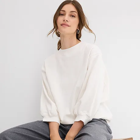Vit oversizesweatshirt med vida ärmar kombinerad med ett par grå byxor.