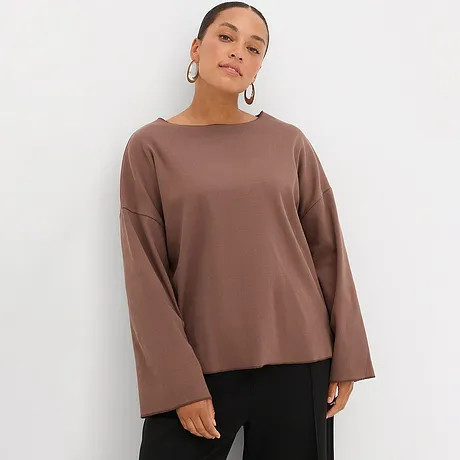 Brun topp med vida, långa ärmar kombinerad med svarta byxor.