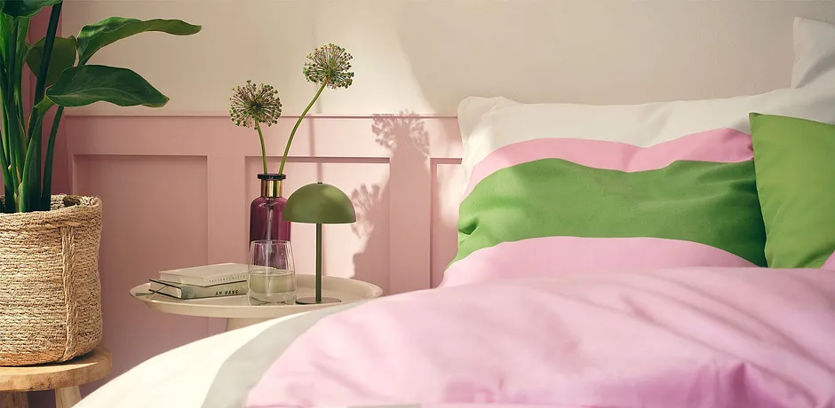 Pastellfärgade sängkläder i rosa och grönt pryder den mysiga sängen i det soldränkta sovrummet.