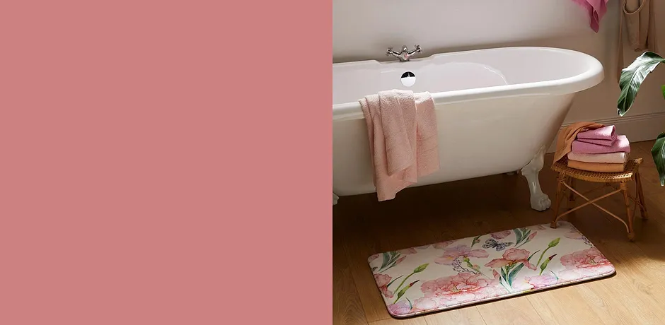 Fräscha handdukar och en blommig badmatta pryder badrummet med ett vitt vintagebadkar.