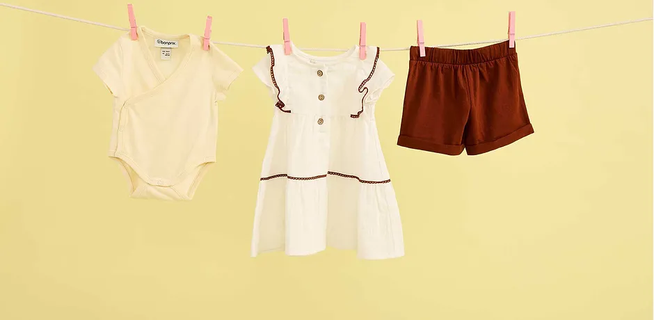 Somriga babykläder på en tvättlina: body, vit klänning och bruna shorts för varma dagar.
