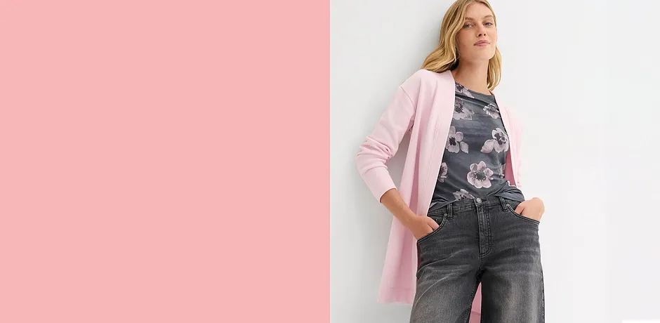 Lång rosa kofta över mörka jeans. Elegant kontrast mellan ljusa och mörka färger.