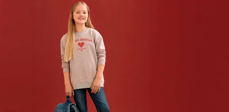 Grå tröja med rött hjärttryck, blå jeans och en jeansväska som accessoar.