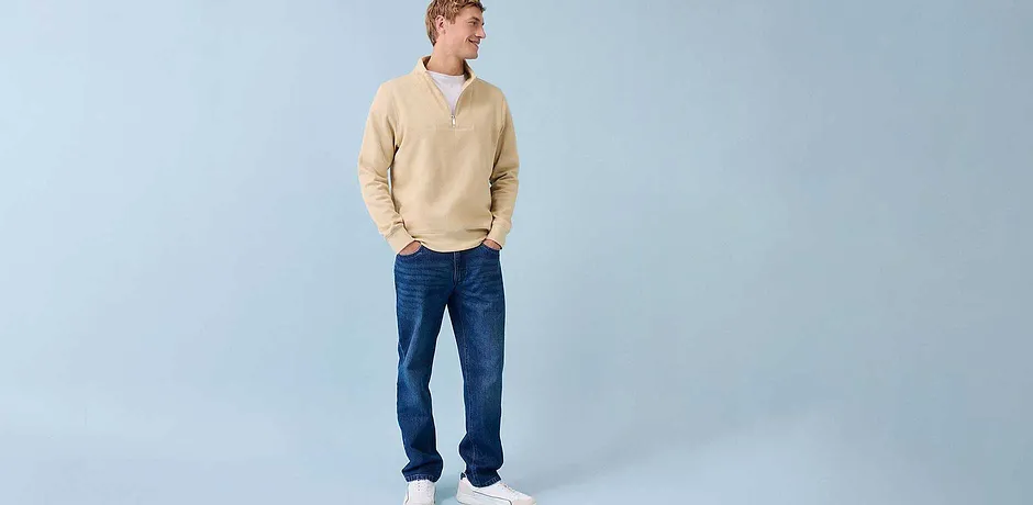 Avslappnad look med krämfärgad tröja, blå jeans och vita sneakers.