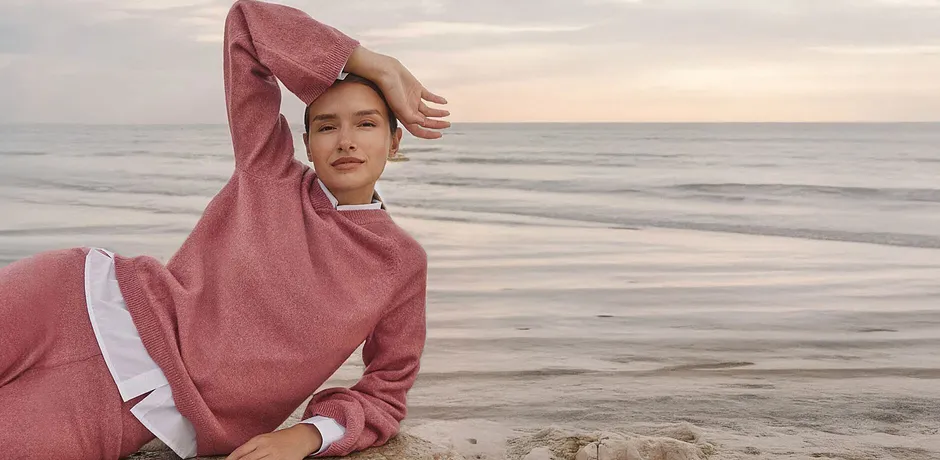 Kvinna i rosa stickad tröja vid havet, bekväm loungewear-look.