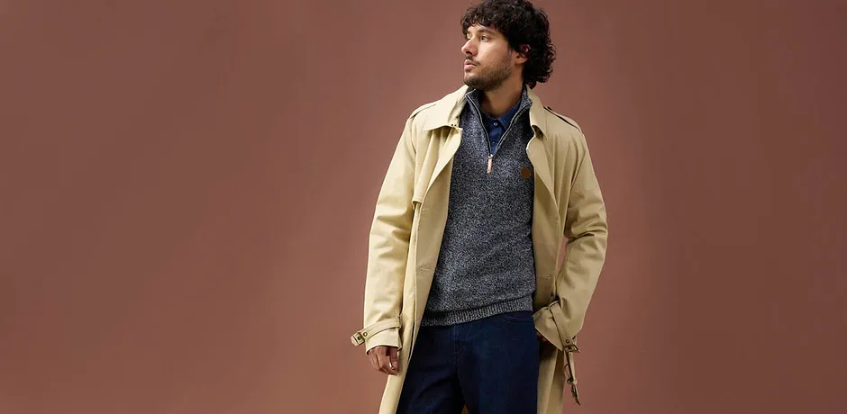 Beige trenchcoat över blå-grå stickad tröja och jeans - avslappnad höstlook för kalla dagar.

