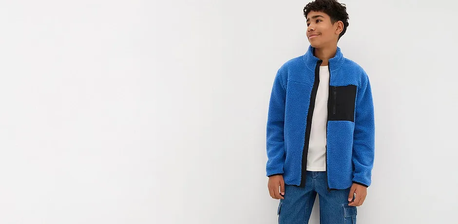 En blå fleecetröja med svart infällning kombinerad med jeans och vit T-shirt.