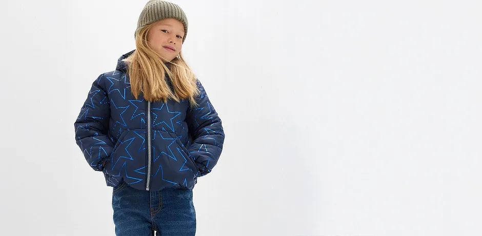 Blå vadderad jacka, jeans och en skön grön mössa.