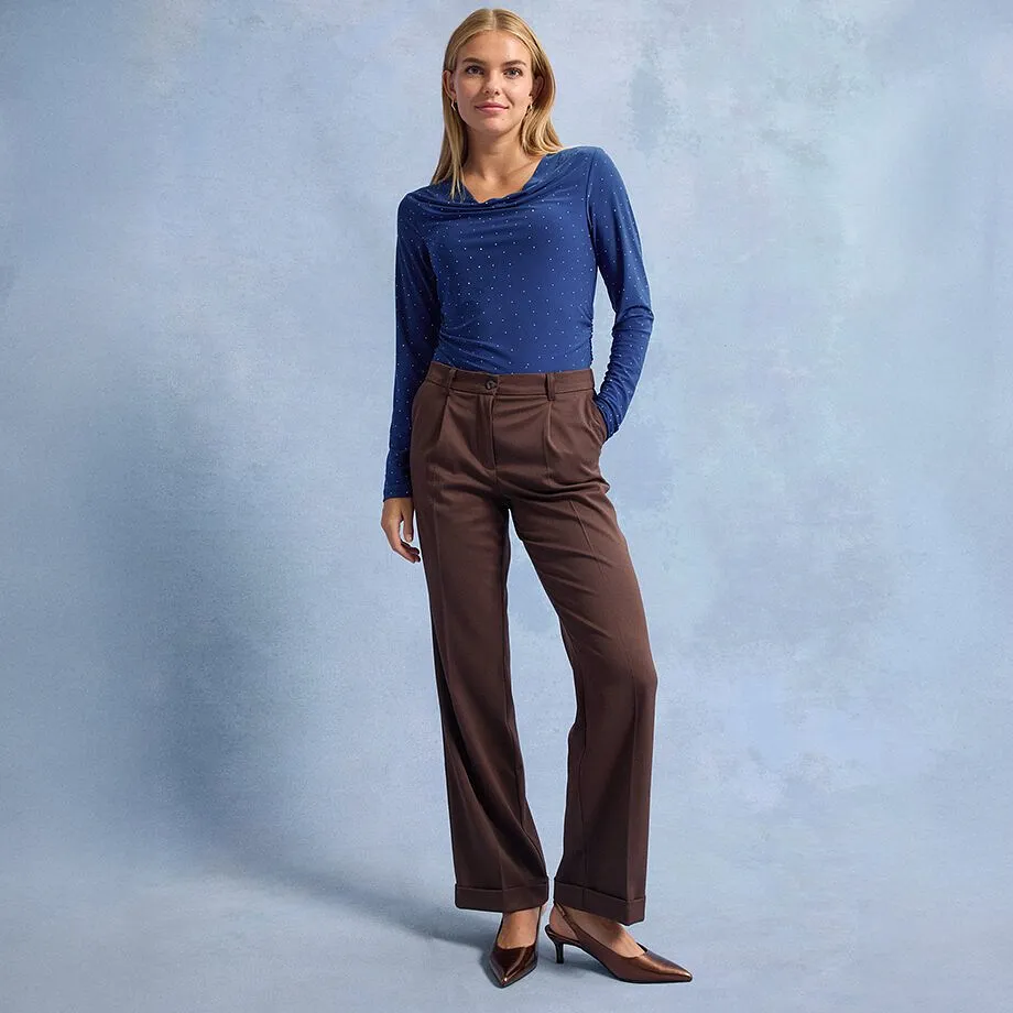 Bl&aring; l&aring;ng&auml;rmad tr&ouml;ja med prickar, bruna byxor med vida ben och spetsiga bruna skor.

