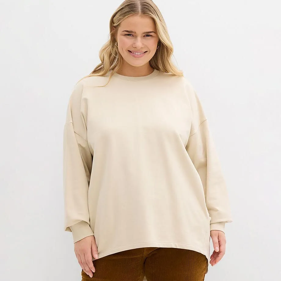 Krämfärgad sweatshirt med rund halsringning, kombinerat med bruna byxor.

