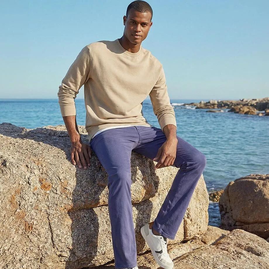 Beige tr&ouml;ja och bl&aring;lila byxor harmoniserar perfekt med havsmilj&ouml;n i bakgrunden.

