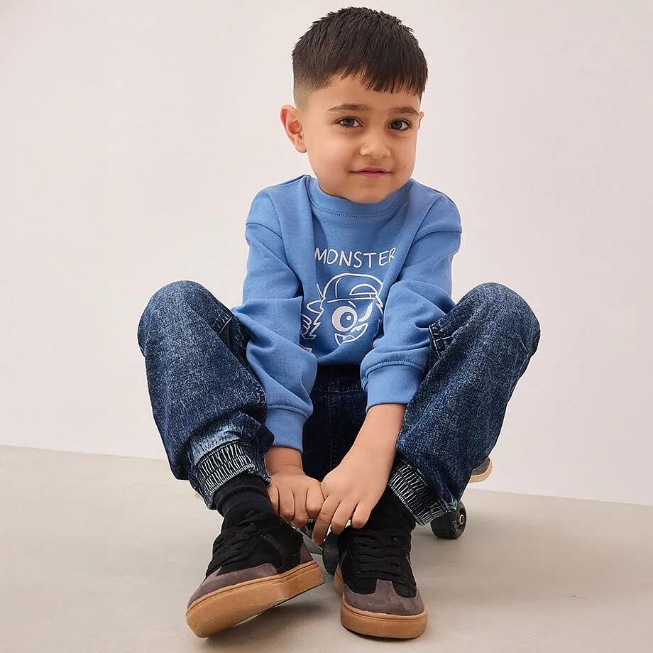 Bl&aring; tr&ouml;ja med monstermotiv, m&ouml;rka jeans och svarta sneakers.

