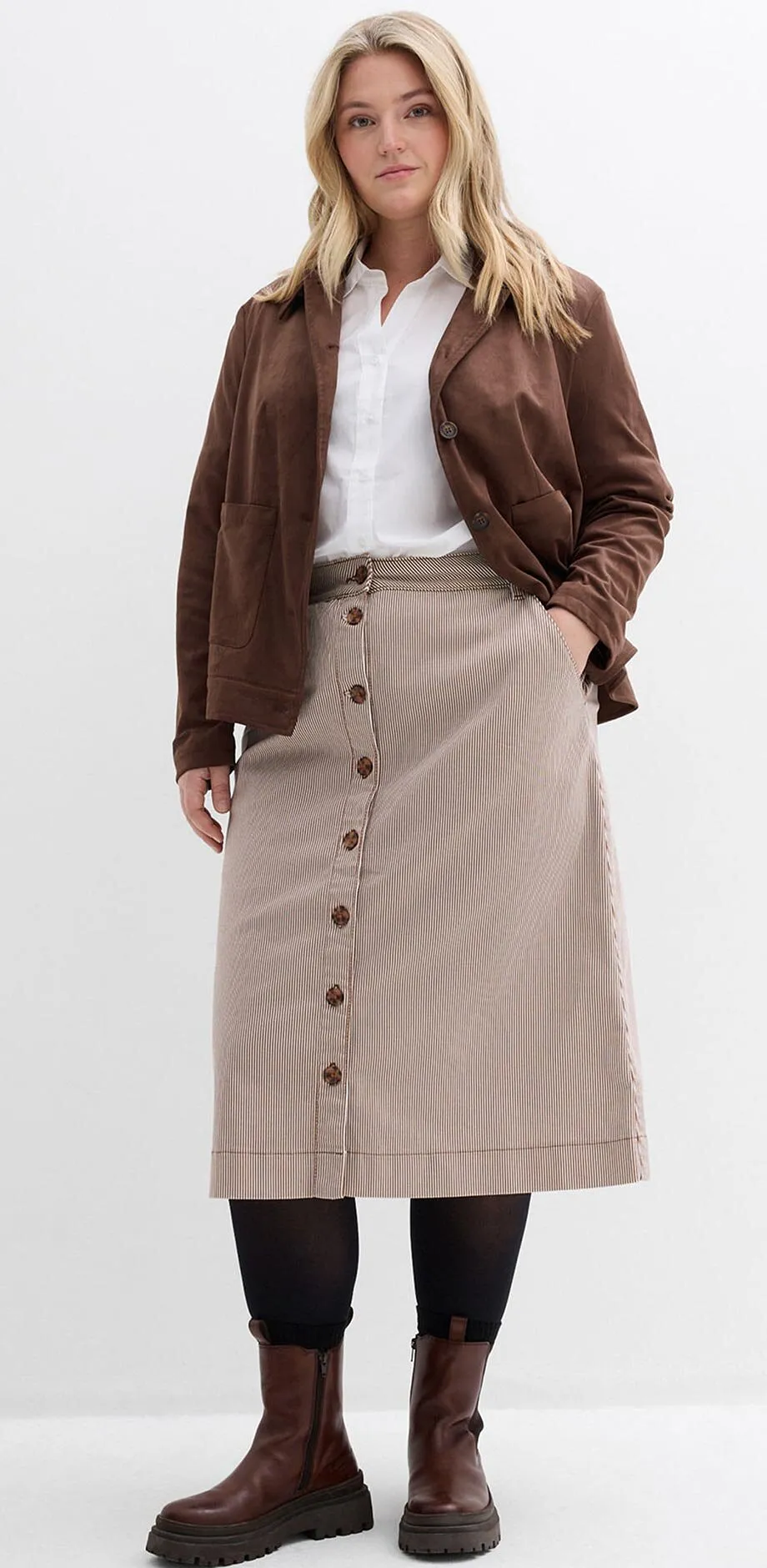 Brun jacka, vit blus, randig kn&auml;ppt kjol och bruna st&ouml;vlar.

