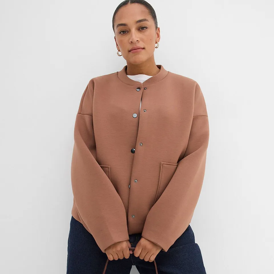 Jacka i terrakotta med tryckknappar och rund halsringning.

