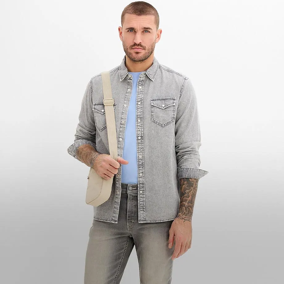 Ljus jeansskjorta &ouml;ver en ljusbl&aring; T-shirt, med gr&aring; jeans och en beige axelremsv&auml;ska.

