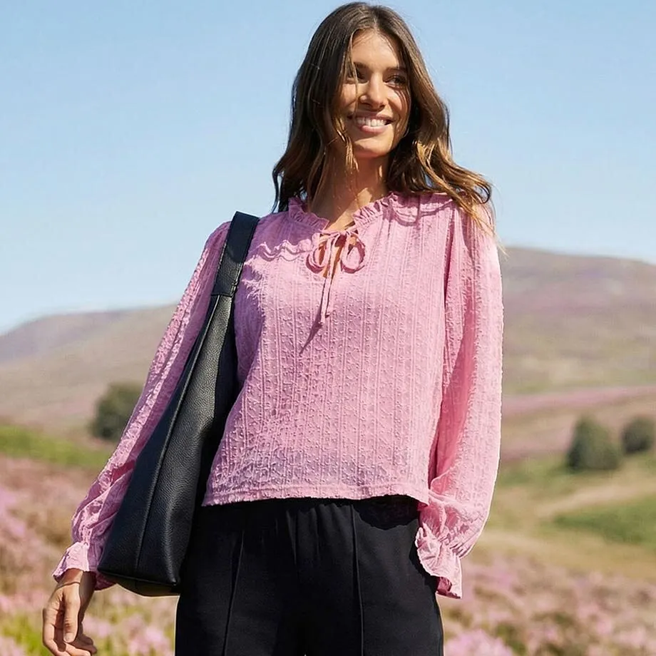 Rosa l&aring;ng&auml;rmad tr&ouml;ja med knytkrage, luftiga &auml;rmar och svarta byxor.

