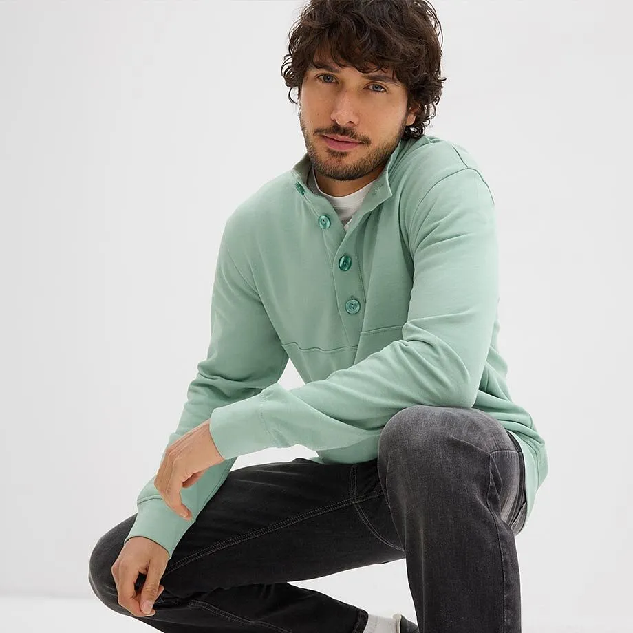 Mintgr&ouml;n sweatshirt med knappar, vit tr&ouml;ja under och m&ouml;rka jeans.

