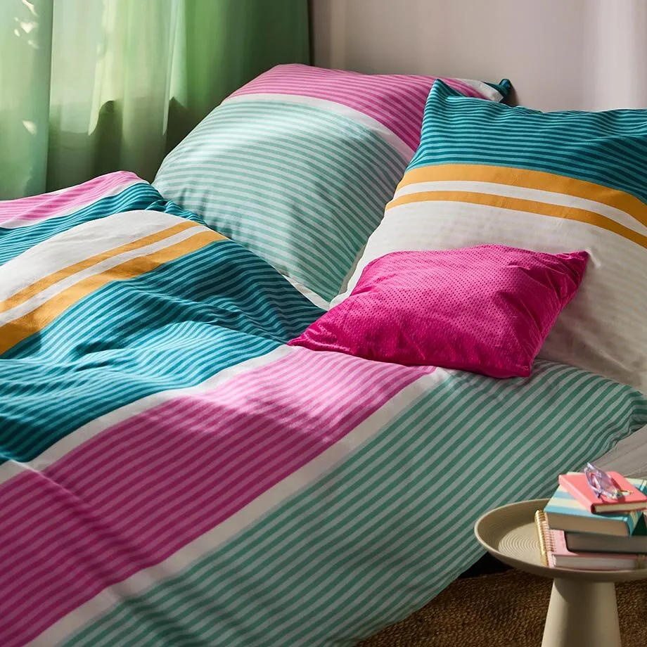 F&auml;rgglada s&auml;ngkl&auml;der med r&auml;nder i rosa, gr&ouml;nt och orange pryder den mysiga s&auml;ngen.

