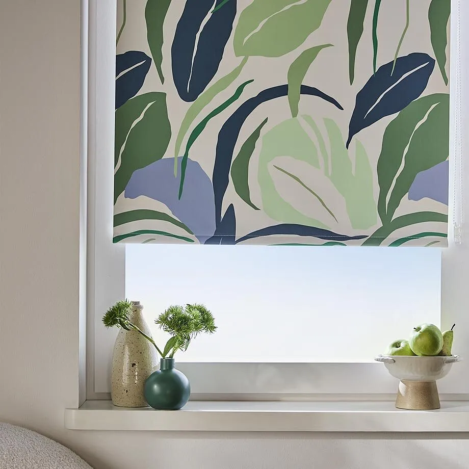 Stilren rullgardin med gr&ouml;nbl&aring; bladm&ouml;nster pryder det ljusa f&ouml;nstret i det moderna vardagsrummet.
