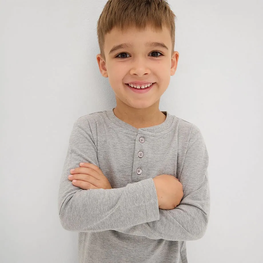 Pojken b&auml;r en gr&aring; l&aring;ng&auml;rmad tr&ouml;ja med knappar vid kragen.

