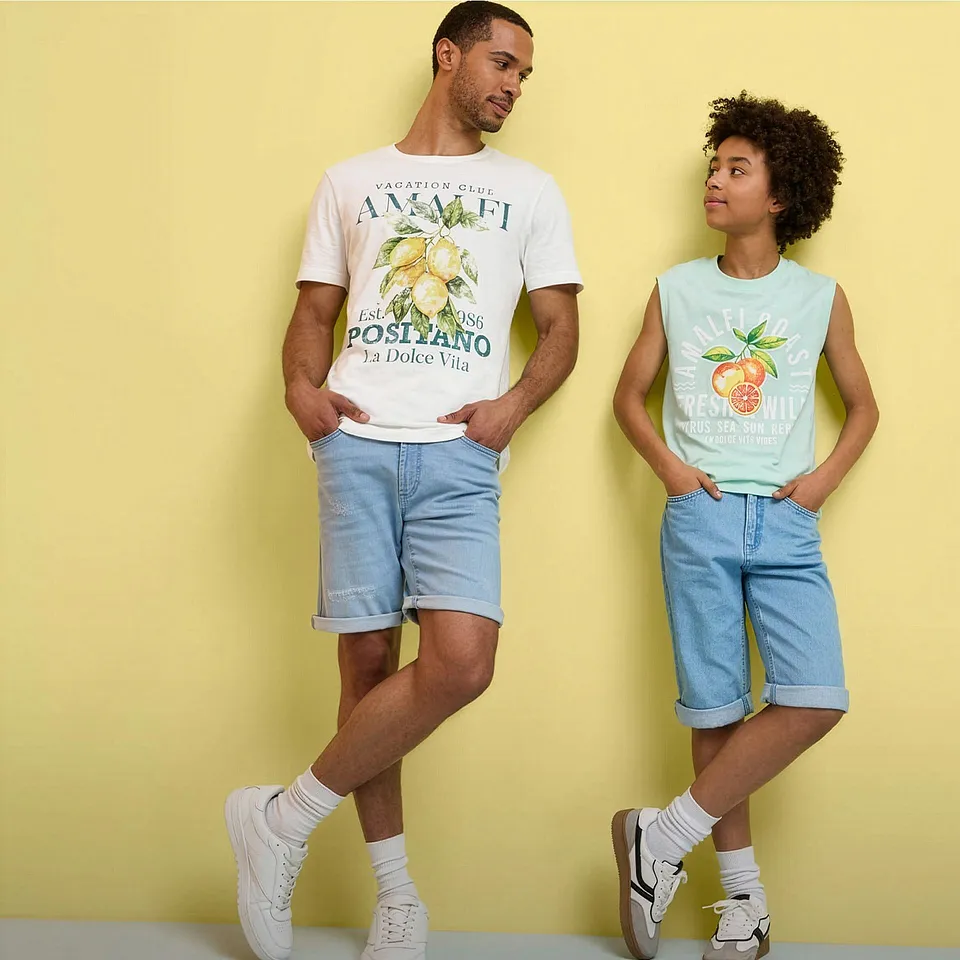 Tv&aring; personer b&auml;r somriga outfits med tryckta t-shirts, jeansshorts och vita sneakers.

