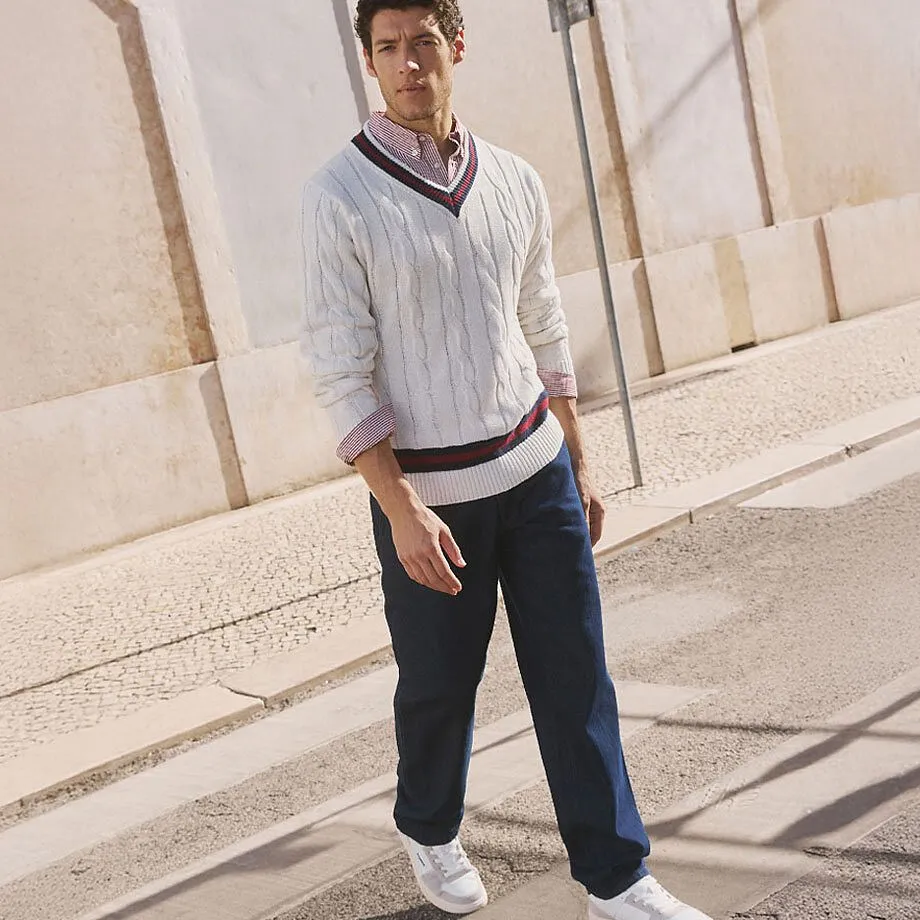 Vit kabelstickad tr&ouml;ja &ouml;ver skjorta, m&ouml;rka byxor och vita sneakers.

