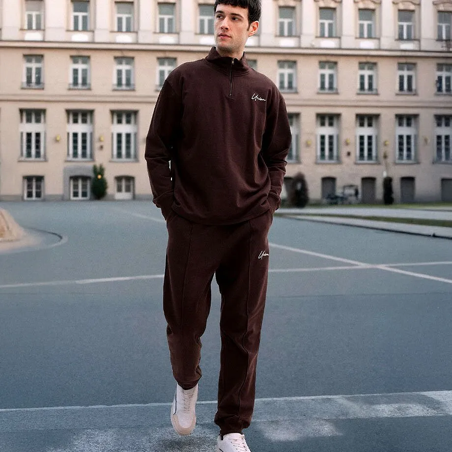 M&ouml;rkbrun tr&auml;ningsoverall och vita sneakers.

