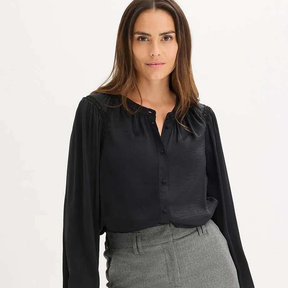 Elegant svart blus med V-ringning, kombinerad med ett par gr&aring; byxor.

