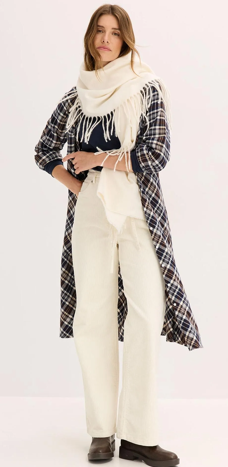 Rutig kappa &ouml;ver en cremef&auml;rgad outfit med polotr&ouml;ja, bred halsduk och byxor.

