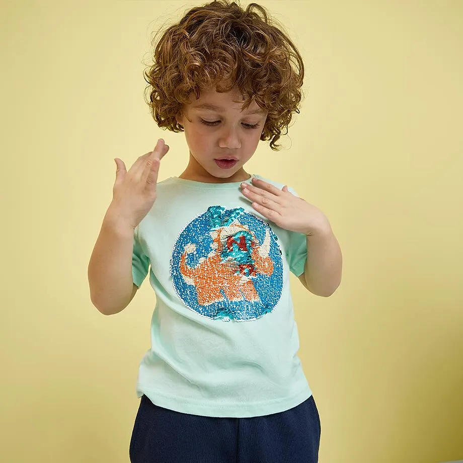 Ett barn i turkos T-shirt med f&auml;rgglatt tryck.