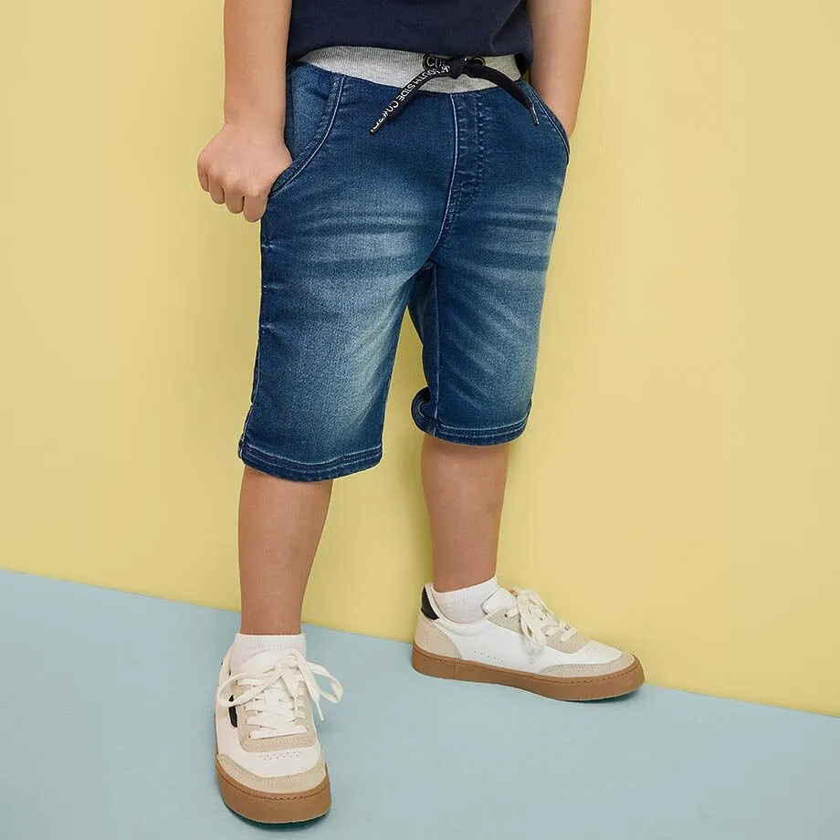 Ett barn b&auml;r bl&aring; jeansshorts och vita sneakers.