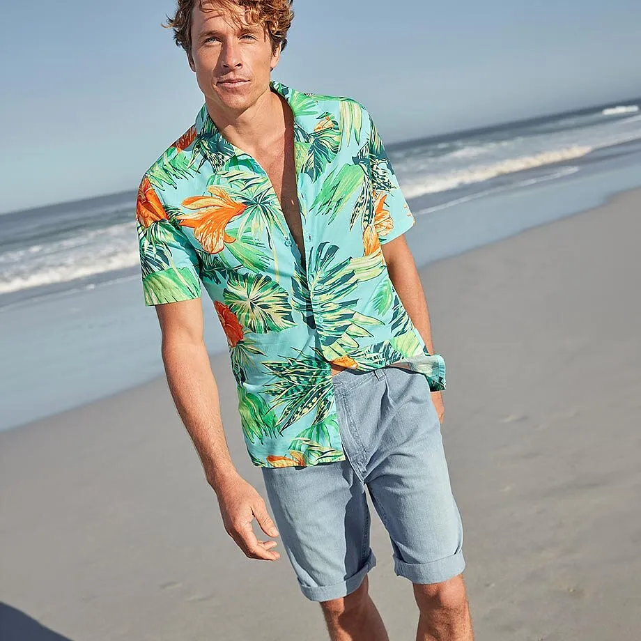 En man b&auml;r en f&auml;rgglad hawaiiskjorta och ljusa shorts p&aring; stranden.

