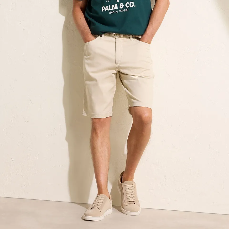 Gr&ouml;n t-shirt med tryck, beige chinosshorts och ljusa sneakers.

