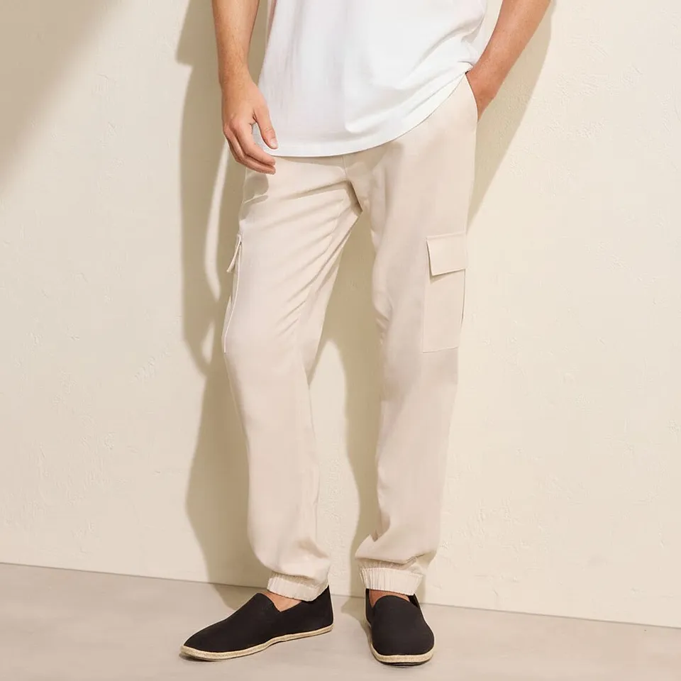 Avslappnad look med en vit t-shirt, beige cargobyxor och m&ouml;rka slip-on-skor.

