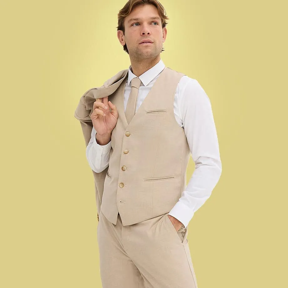 En man b&auml;r en beige kostym med en vit skjorta och matchande v&auml;st.

