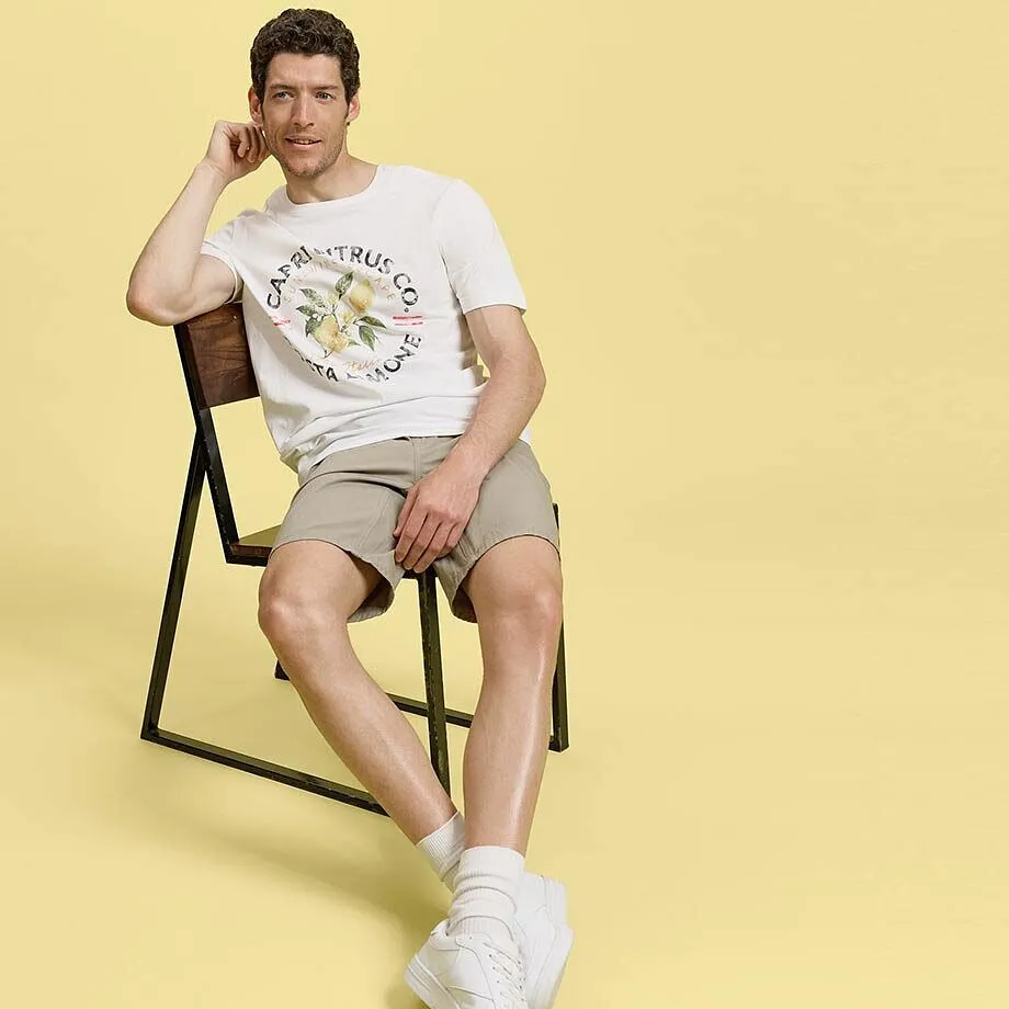 En avslappnad sommaroutfit: vit T-shirt, beige shorts och vita sneakers.